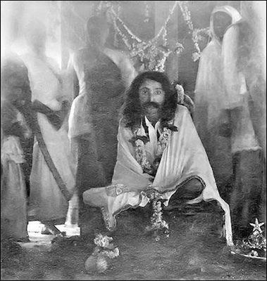 Seated with garlands among white-robed figures.