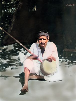 Poona, India. Meher Baba playing an Indian instrument outside his thatched hut.