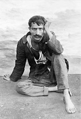 Seated on the ground in dark coat and white pants.